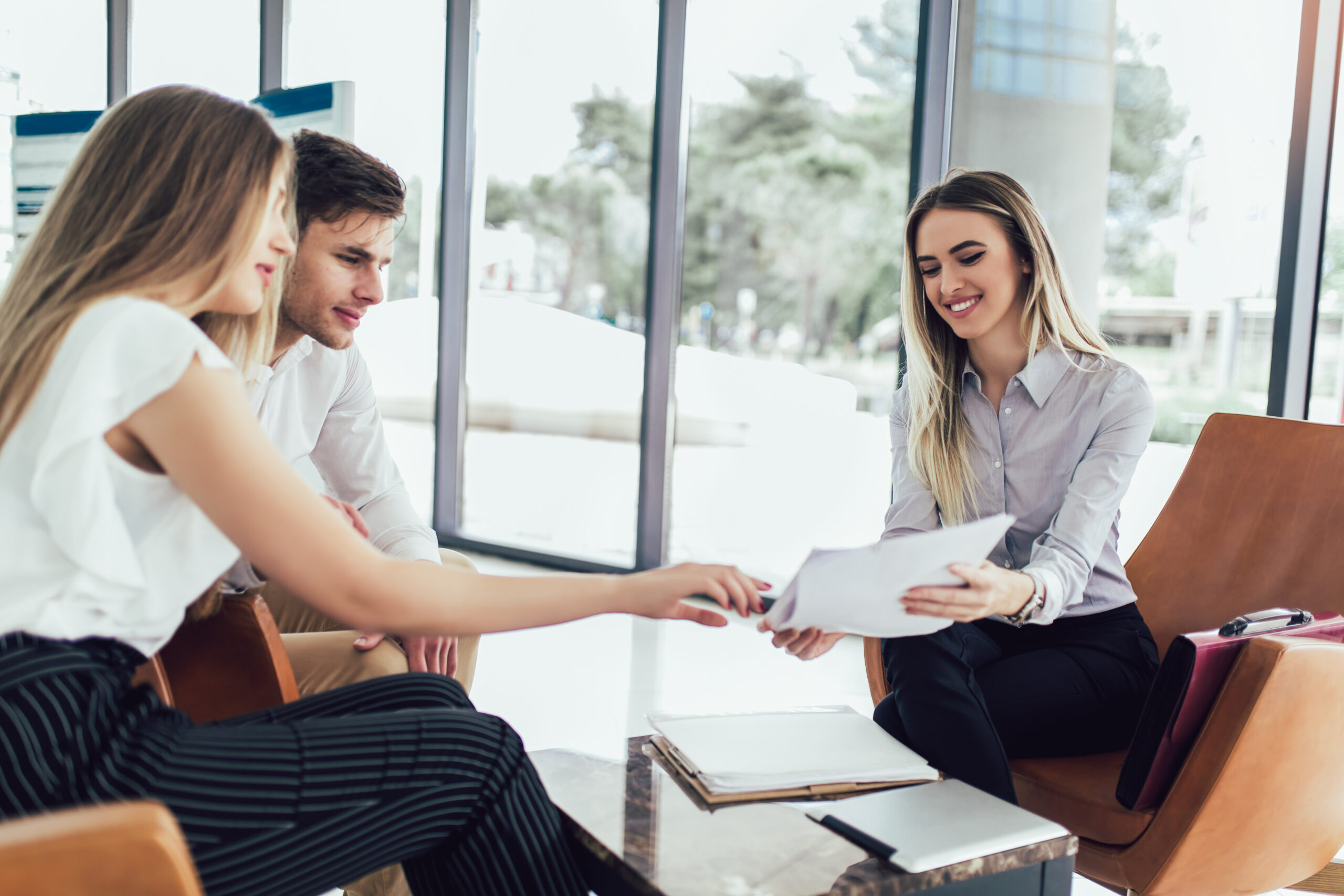 Financial advisor showing report to young couple. Happy couple consulting financial agent for refinance mortgage loan rates to prepare them for buying a home.