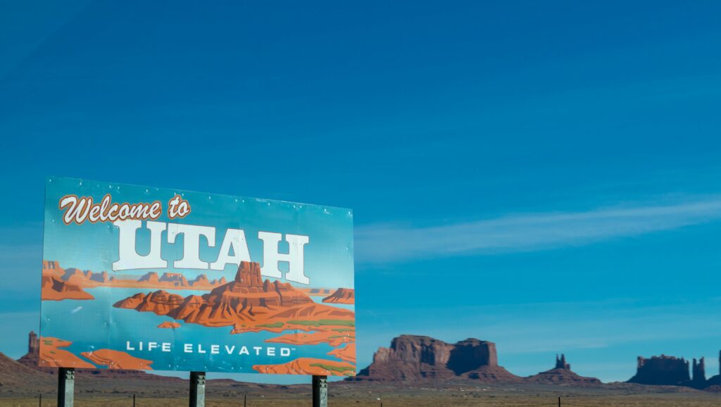 Blue sky with the welcome to Utah sign on the left showing red mountains.