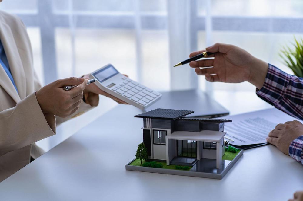 Mortgage advisor showing calculator to client with house model on desk — Utah home loan pre-approval